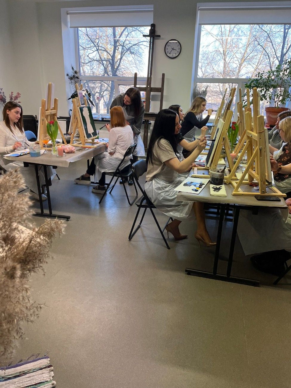 Darba kolektīvs glezno pie galdiem un molbertiem mākslas studijas telpā